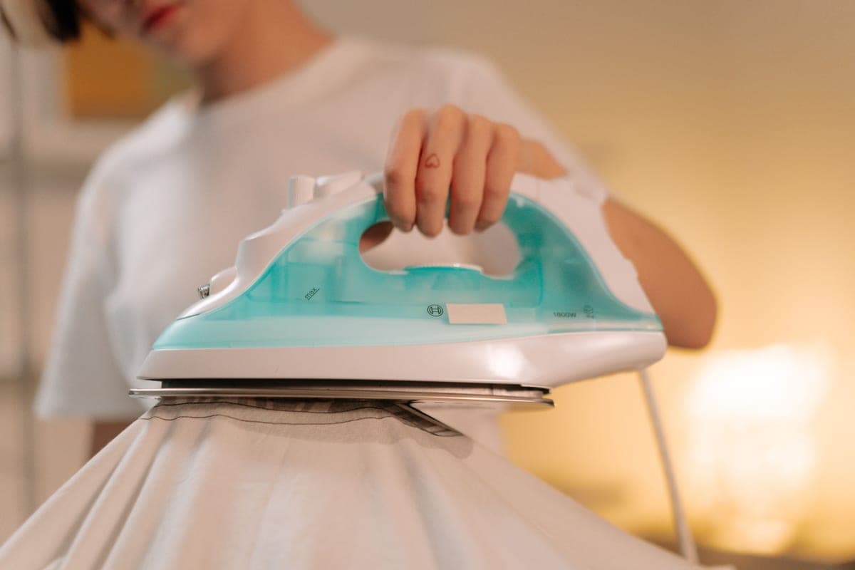A person pressing a white garment flat with a heated plate