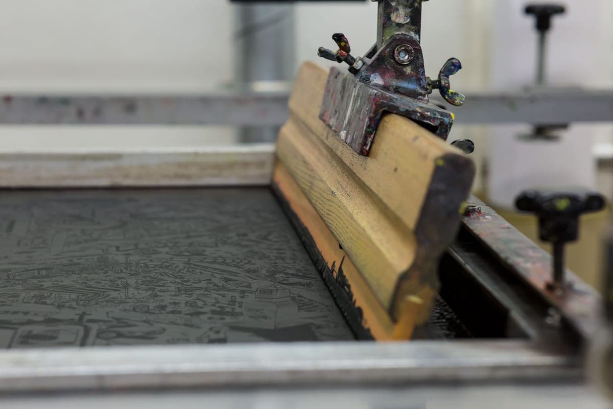 A squeegee pulling ink across a screen printing frame